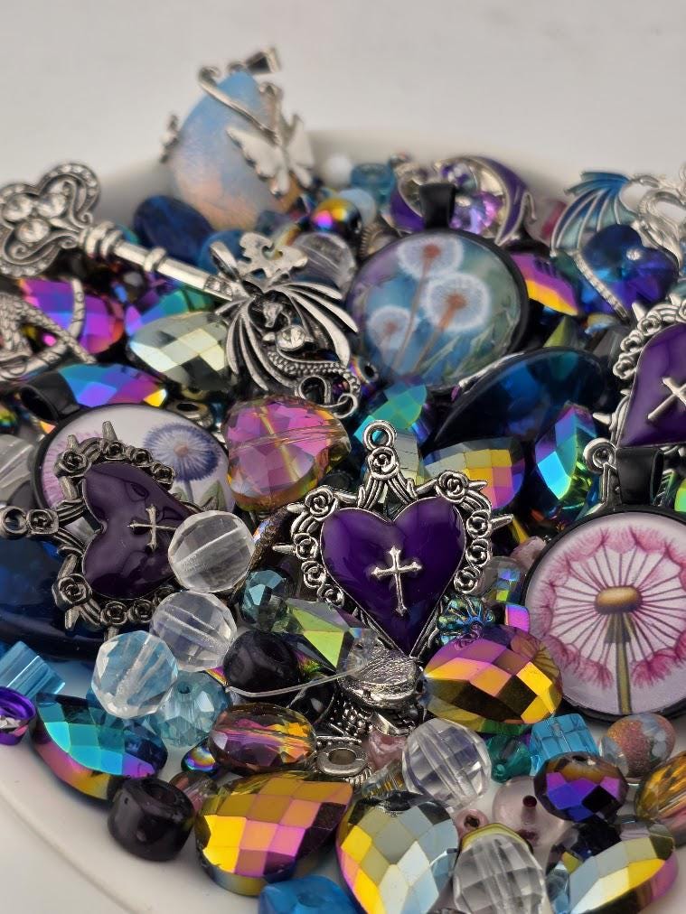 The image is a collection of various colorful beads, charms, and trinkets, including heart-shaped charms, gemstones, and other decorative elements, all arranged on a surface.