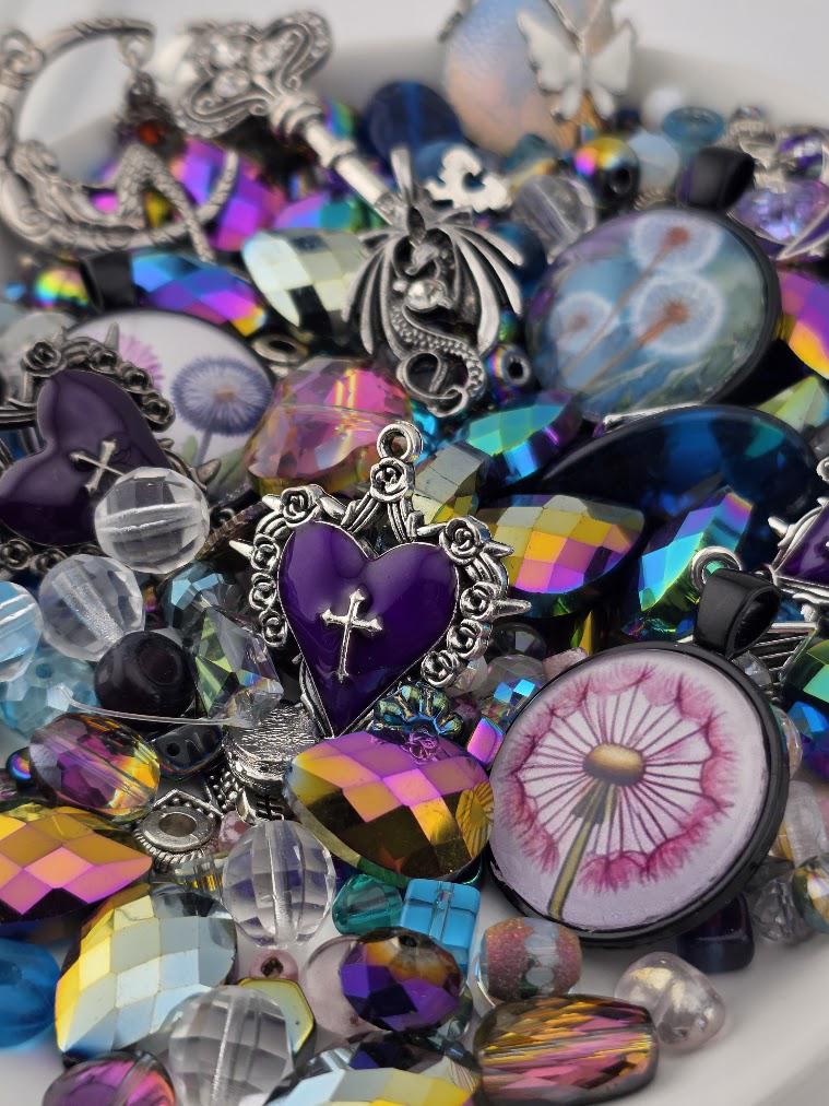 The image is a colorful assortment of various beads, charms, and trinkets, including a heart-shaped charm, a dandelion-like charm, and other decorative elements.