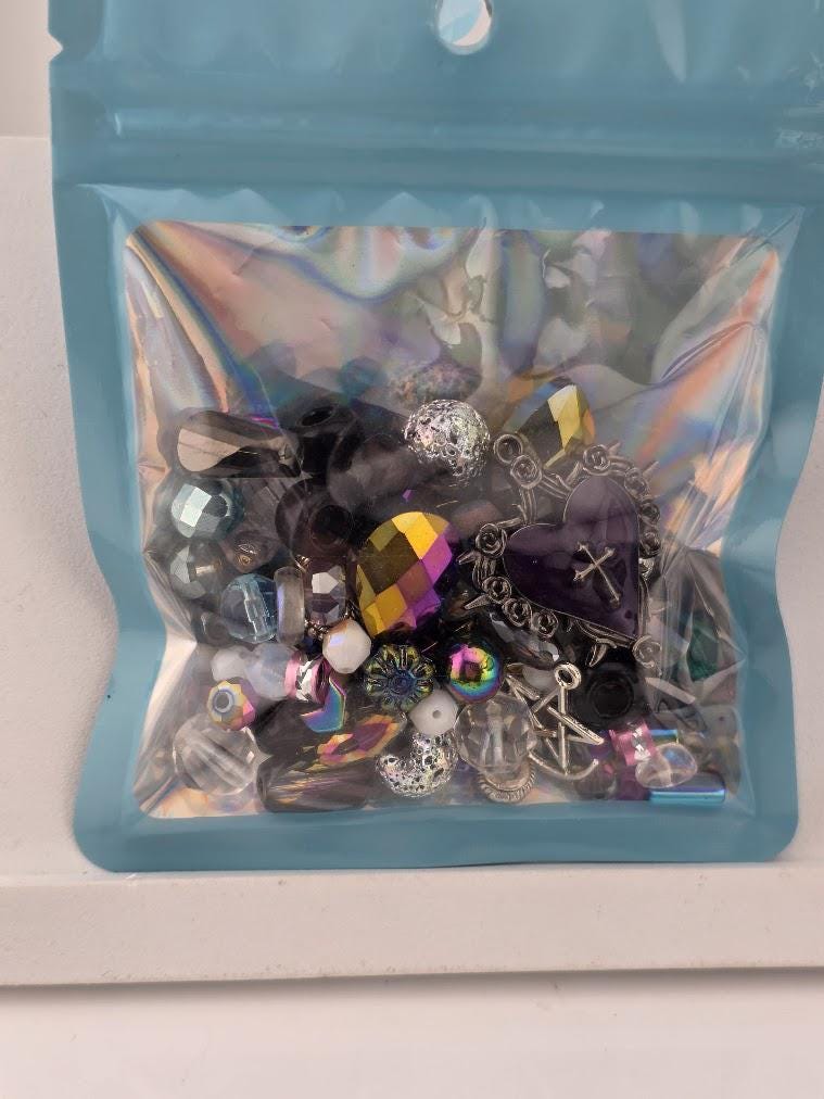 A clear plastic bag filled with various colorful beads, charms, and other small objects.