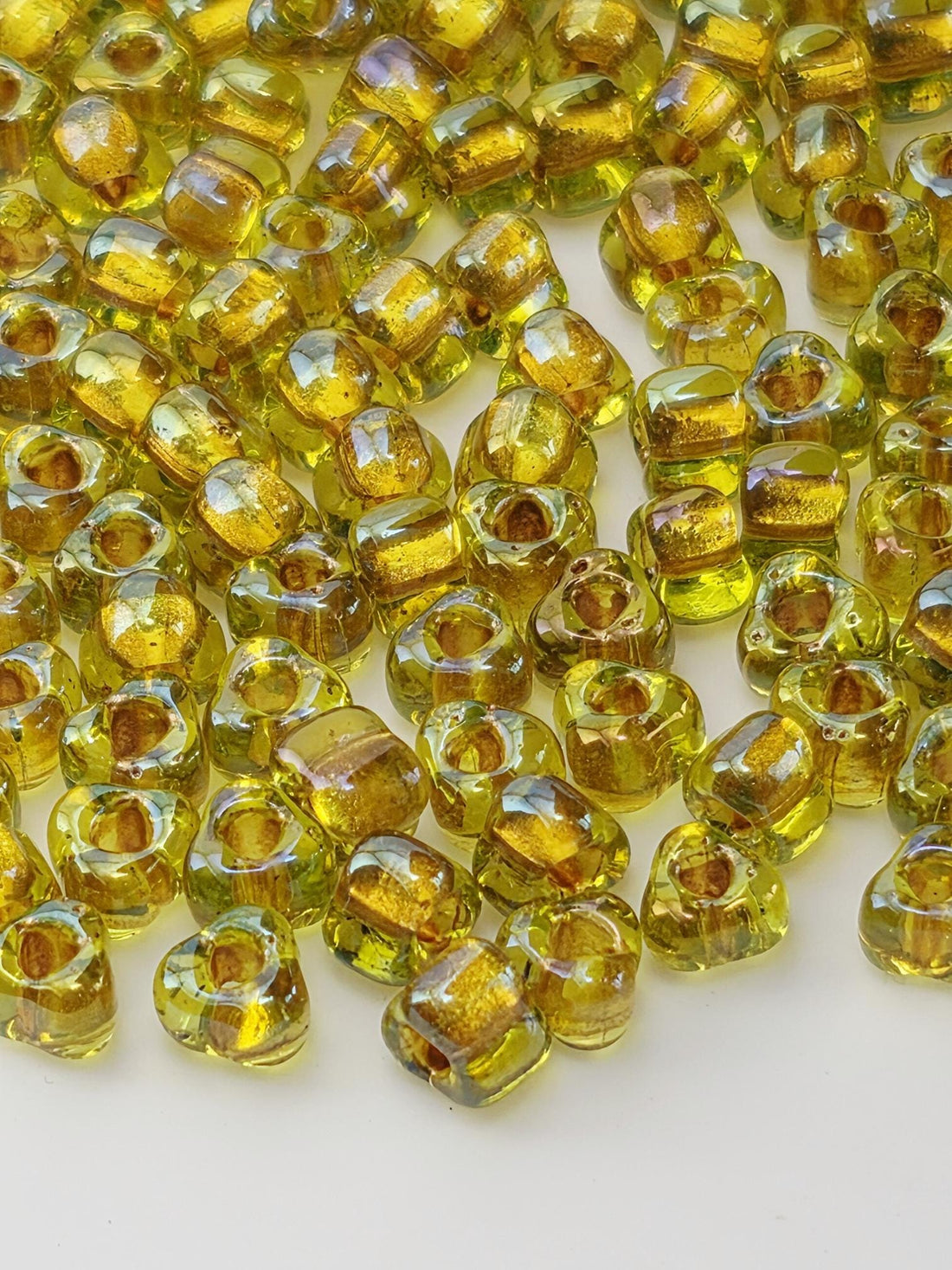 a close-up view of numerous small, clear glass beads in various shades of yellow, scattered across a white surface.