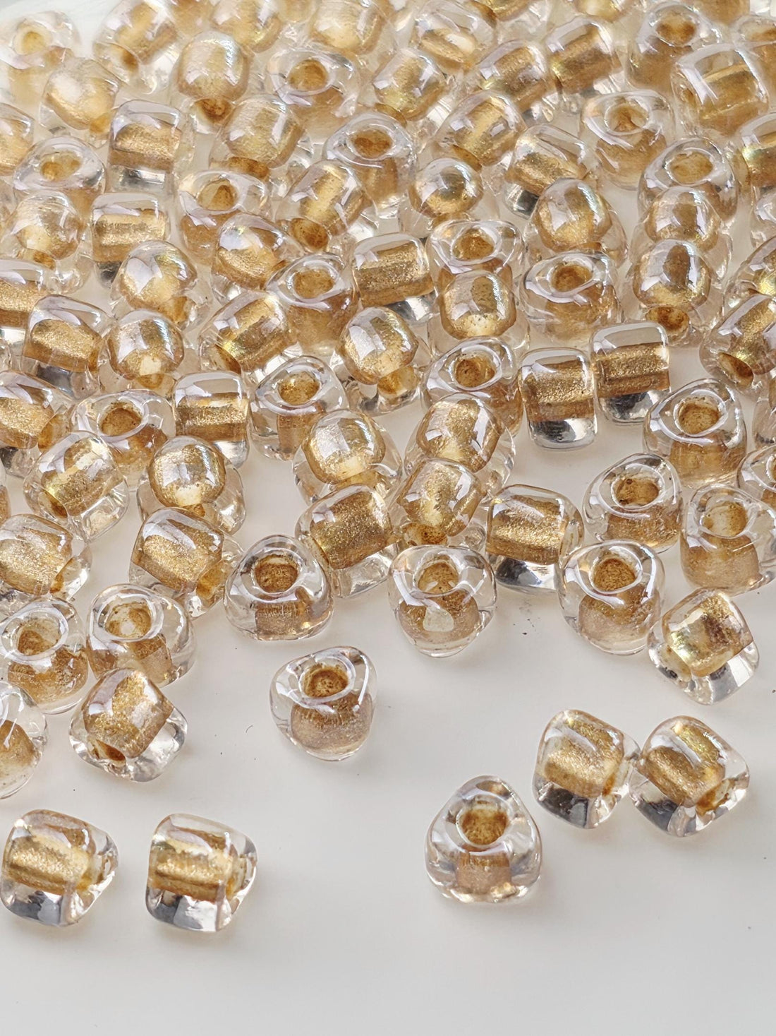 a close-up view of numerous clear glass beads scattered across a white surface. The beads have a golden hue and are arranged in a seemingly random manner, creating a visually striking and intricate pattern.