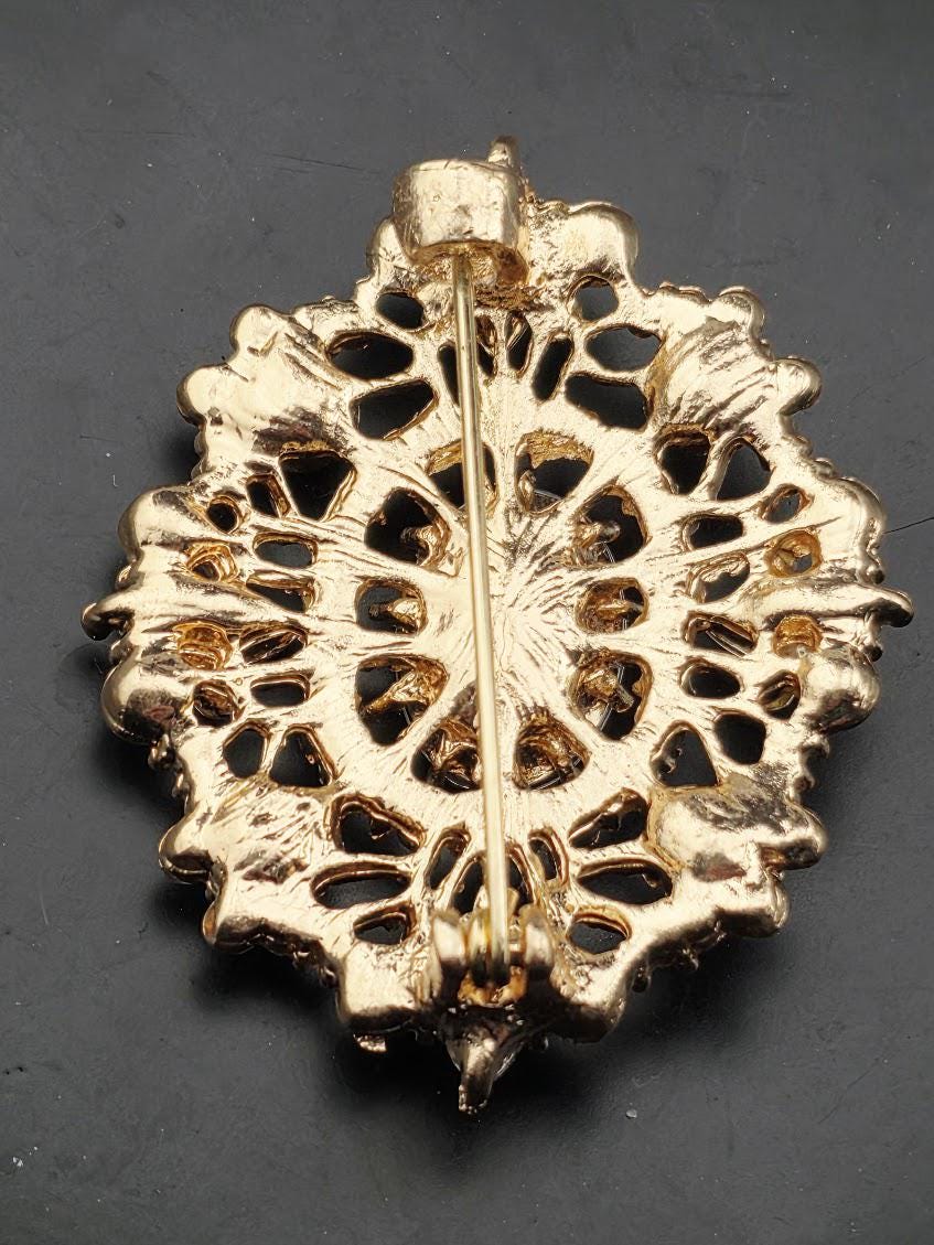 A decorative gold-colored pin or brooch with an intricate floral pattern.