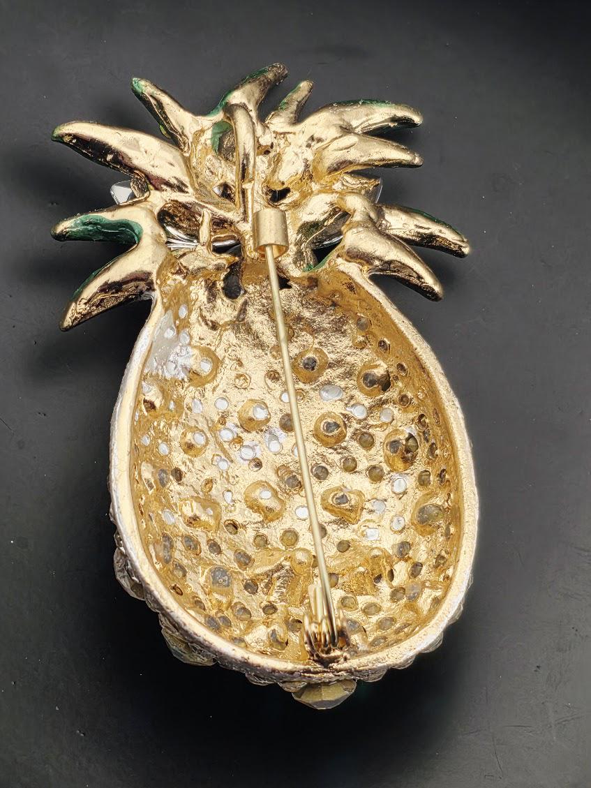 A gold pineapple pin with a decorative design and a metallic stem.