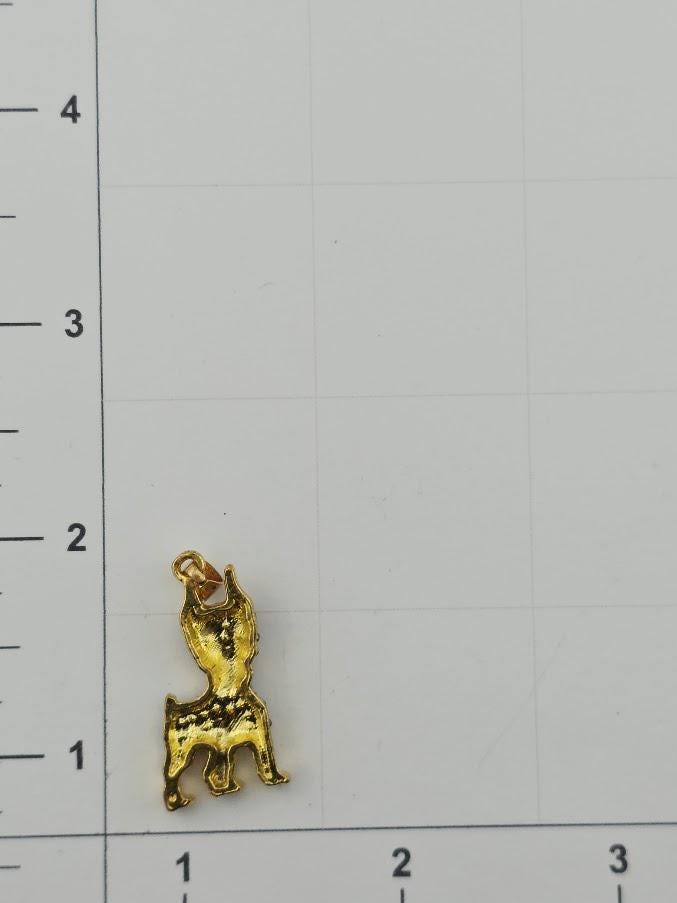 A small gold-colored charm in the shape of a dog is placed on a white grid background.