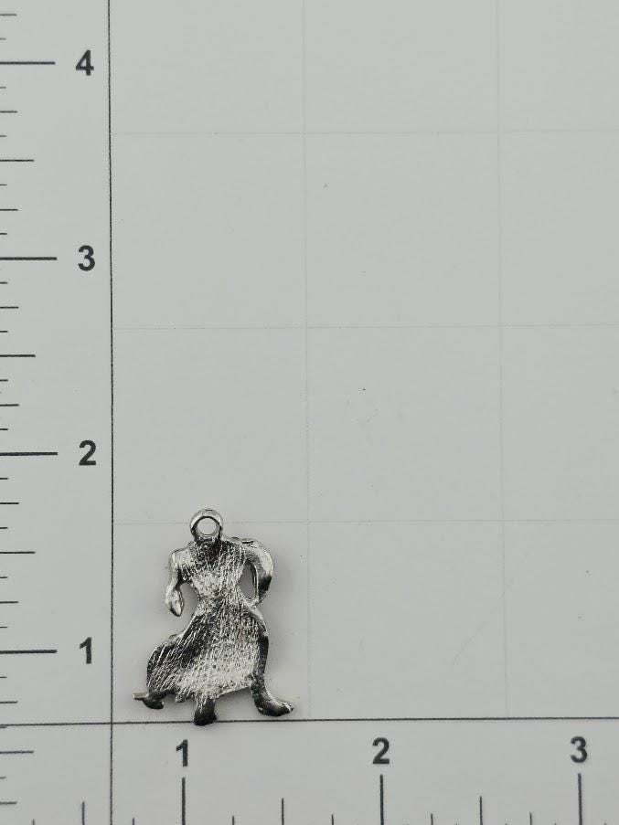 a small metal charm or pendant in the shape of a person, placed on a graph paper background.