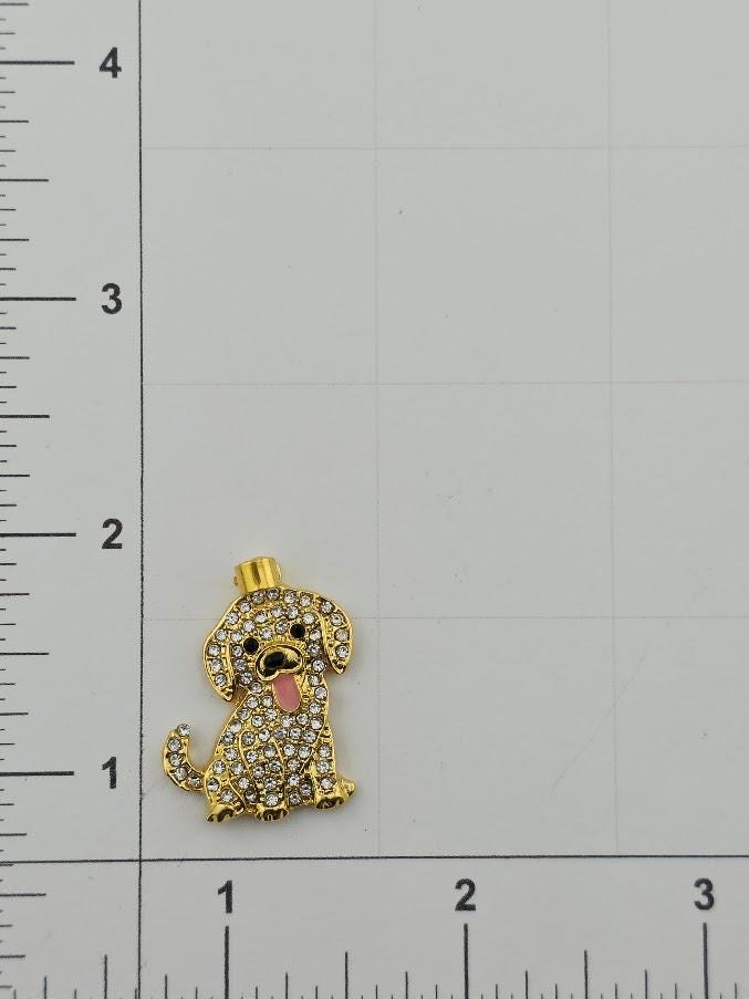 A gold-colored dog-shaped pendant with rhinestones or crystals attached to it, placed on a ruler for size comparison.
