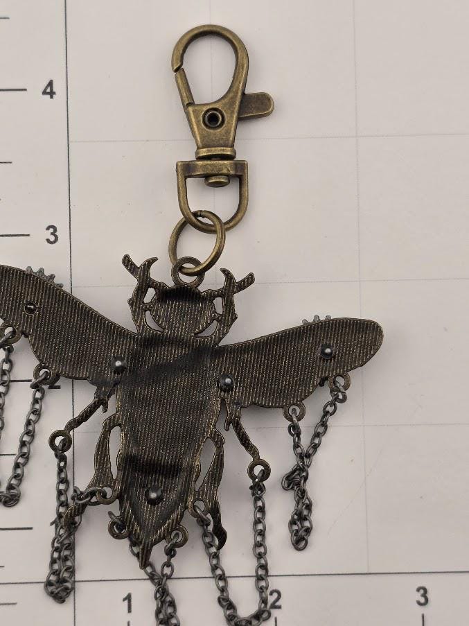 A close-up view of a metal insect-shaped keychain with a chain attached to it.