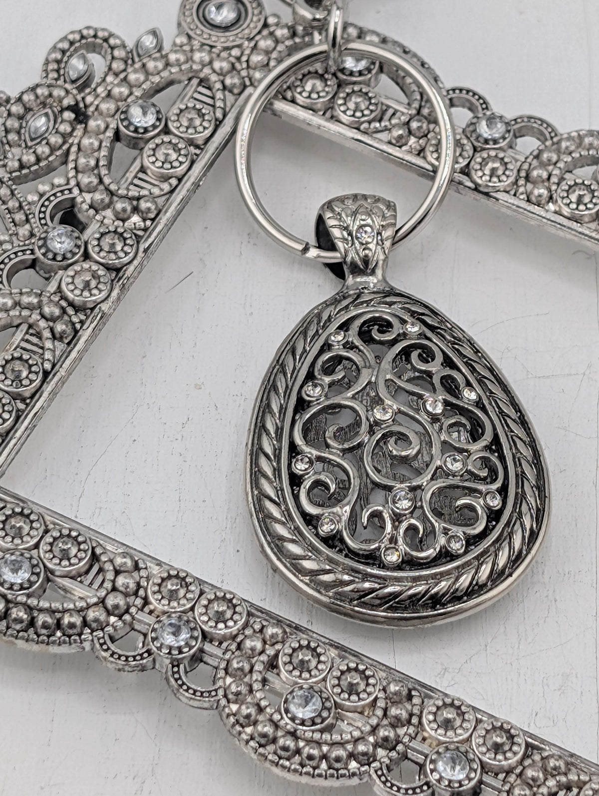 A close-up image of a decorative metal pendant with intricate designs and sparkling crystals.