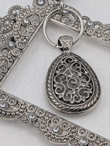 A close-up image of a decorative metal pendant with intricate designs and sparkling crystals.