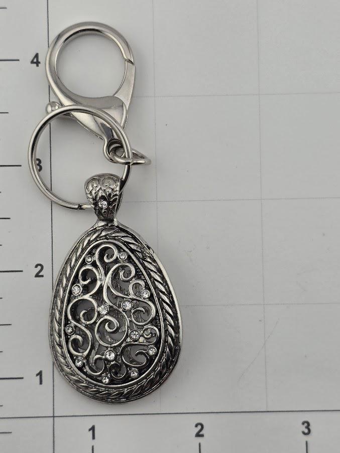 A silver-colored keychain with an oval-shaped pendant featuring a decorative design and small rhinestones or crystals.