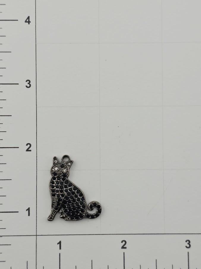 a small black cat charm with a diamond-like pattern on its body, sitting on a white background with a ruler for scale.