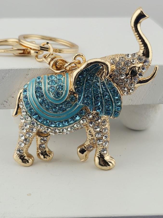 A decorative keychain in the shape of an elephant, with a blue and gold color scheme and sparkling rhinestones or crystals on its body.