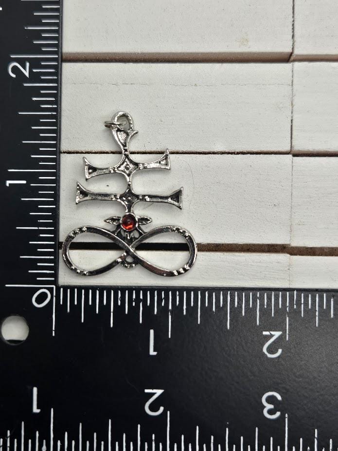 A silver pendant with a red gemstone is placed next to a ruler on a white surface.
