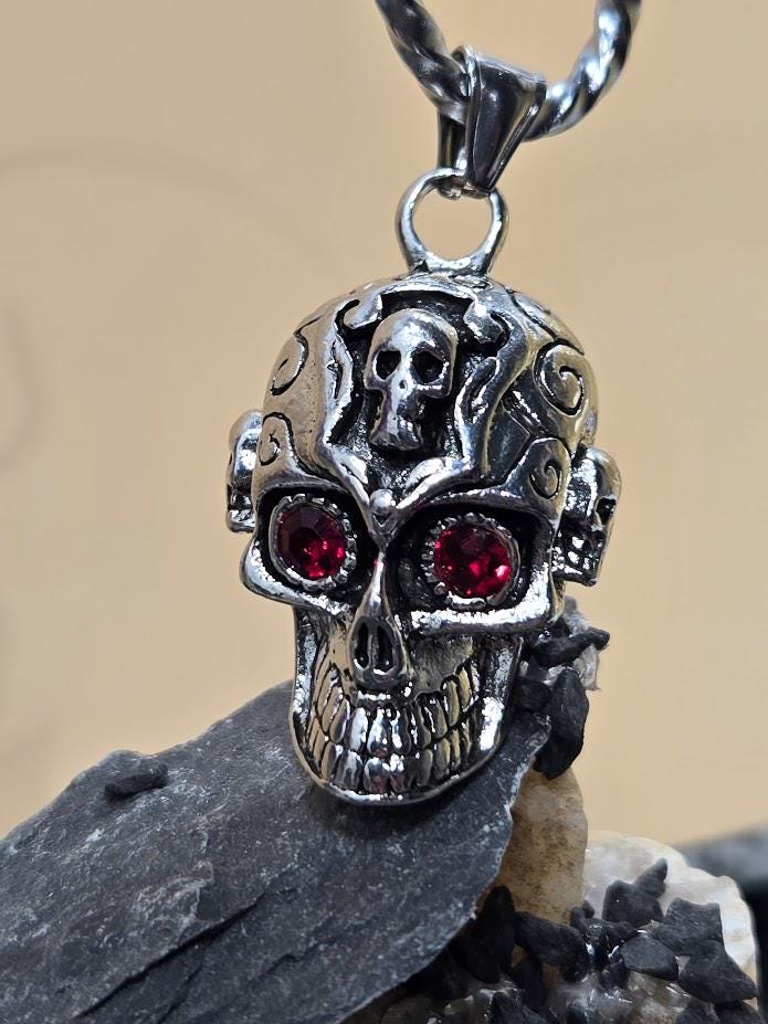 A silver-colored skull pendant with red gemstones, hanging from a chain.
