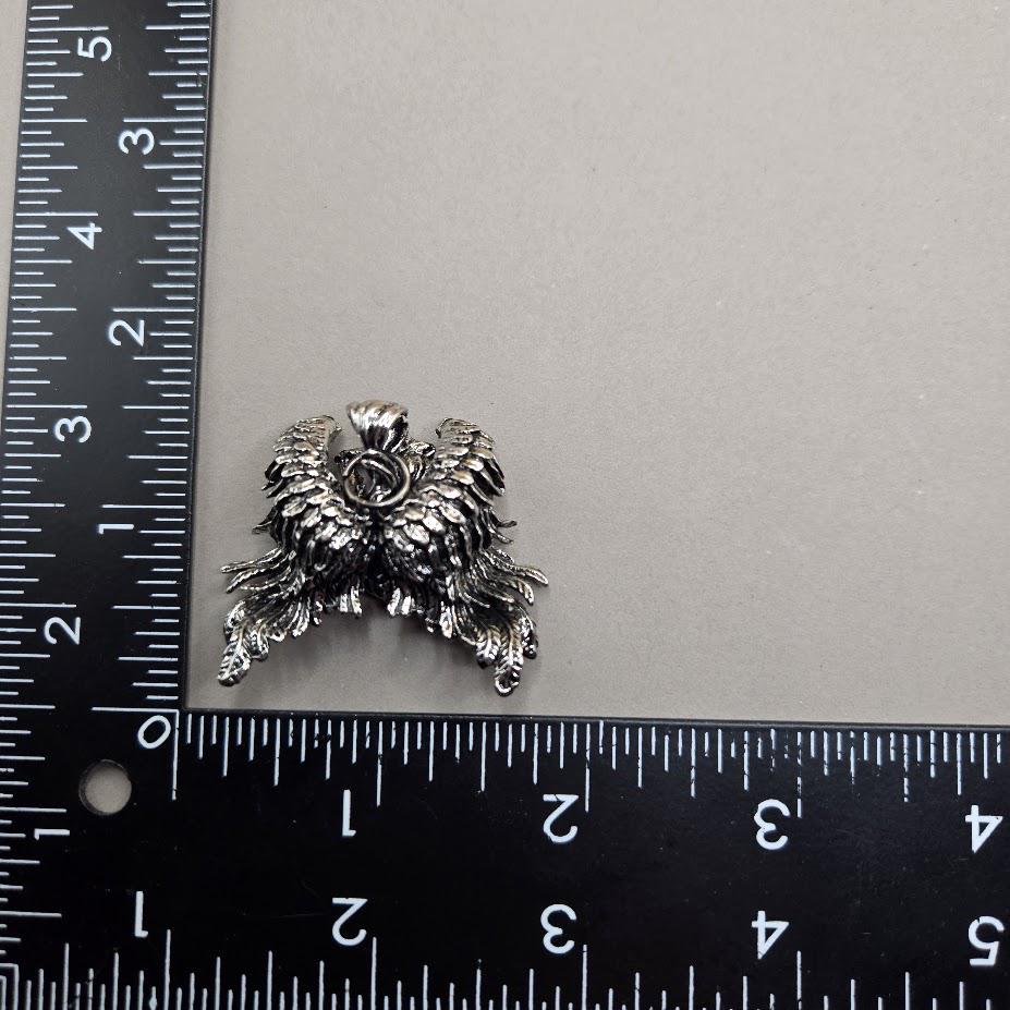 A close-up image of a silver-colored metal object, possibly a piece of jewelry or a decorative item, placed next to a ruler for size comparison.