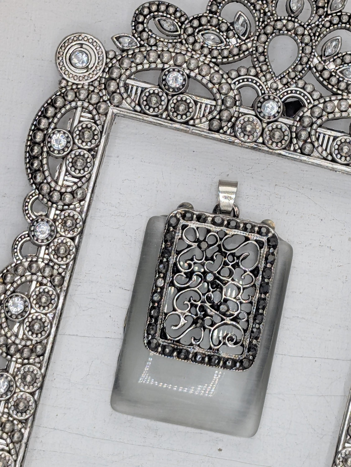 a pendant with a decorative metal design and a glass component, both adorned with small, sparkling stones.