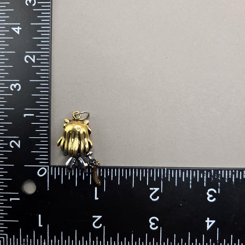 A small gold-colored charm or pendant is placed next to a ruler on a gray surface.
