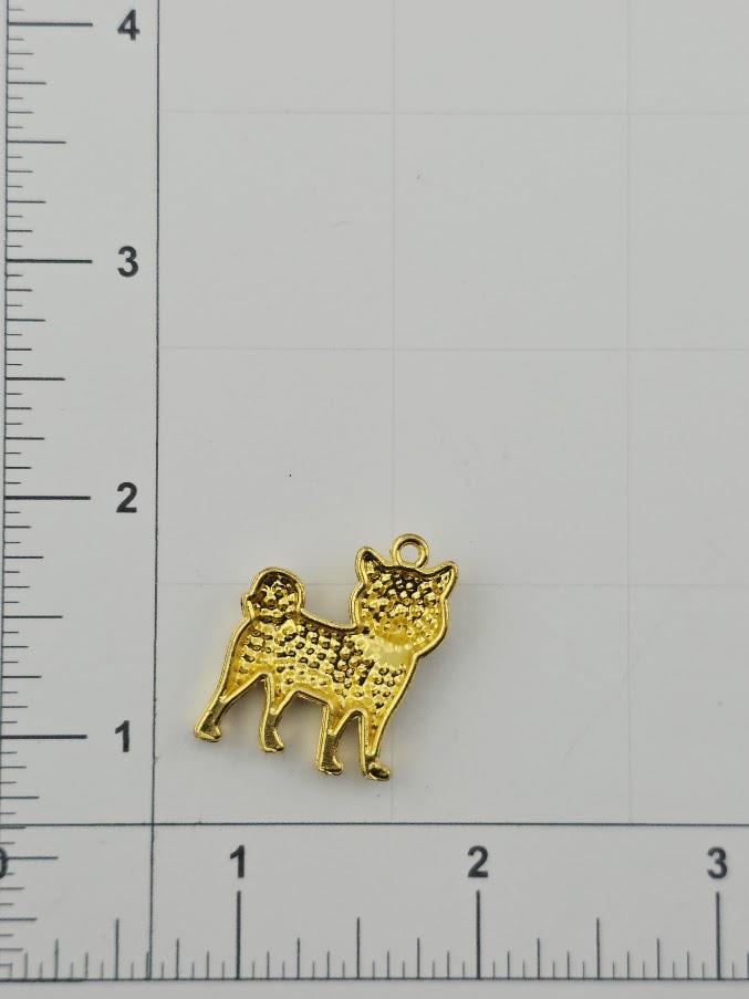 A gold-colored charm in the shape of a dog is placed on a ruler for size comparison.