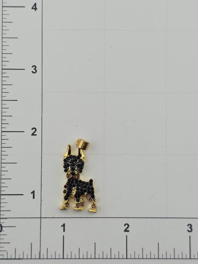 a small gold-colored pendant in the shape of a dog, with black gemstones or stones adorning it. The pendant is placed on a white surface, with a ruler for scale visible in the background.