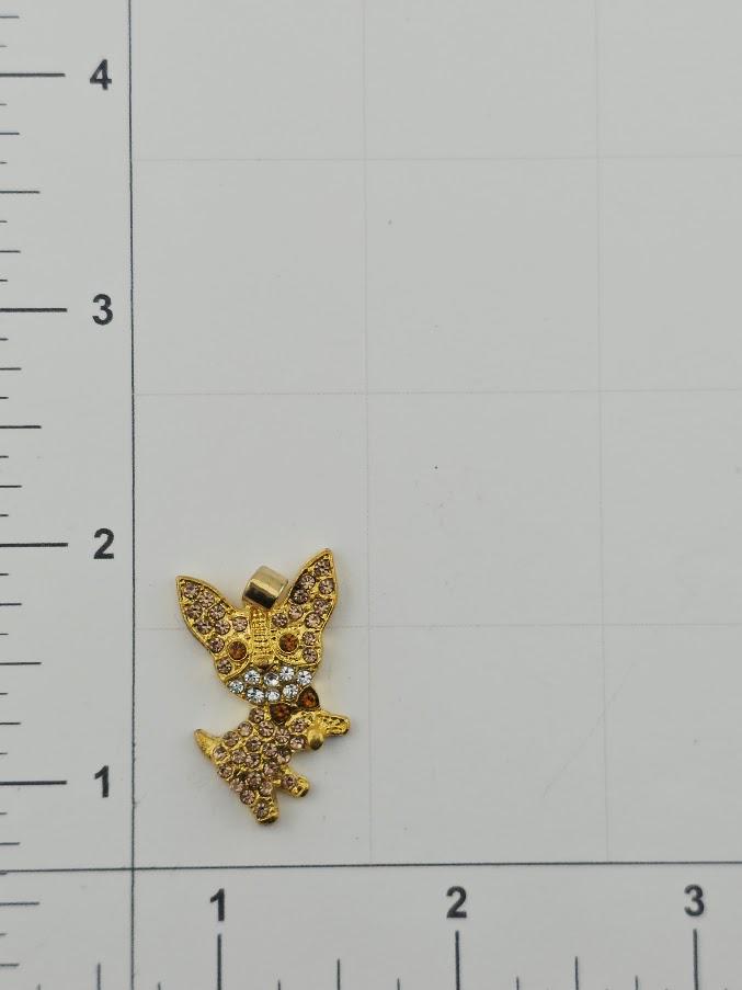 A small gold-colored pendant in the shape of a dog is shown on a white surface, with a ruler for scale.