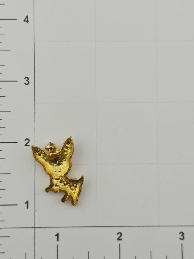 A small golden charm in the shape of a cat is placed on a white surface next to a ruler for size comparison.