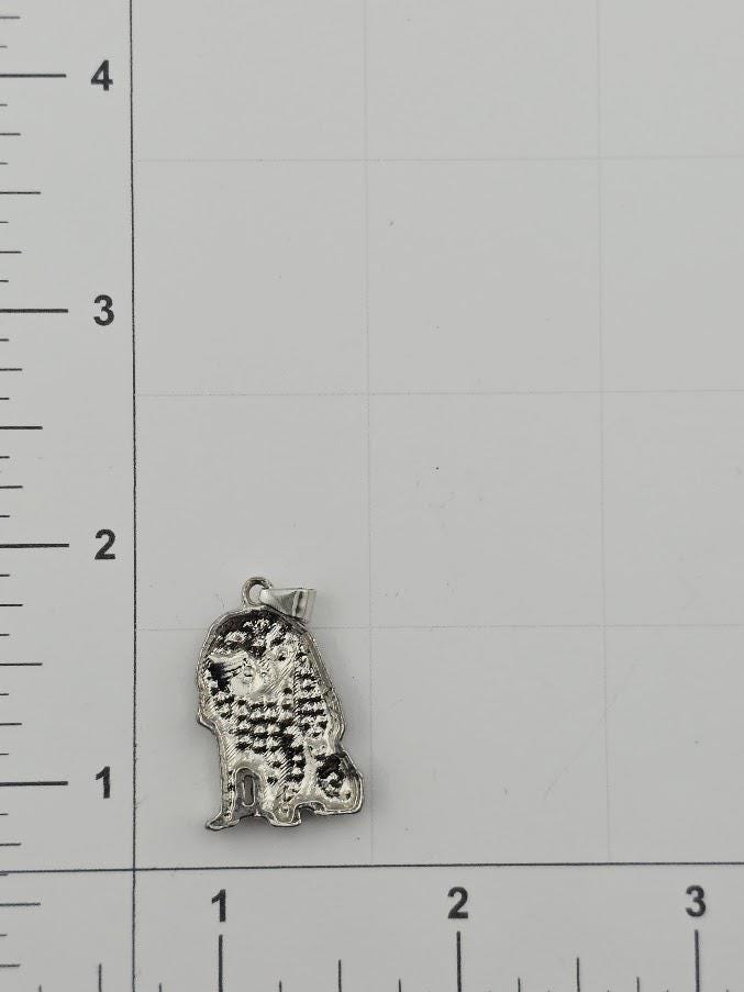 a small silver-colored charm or pendant, which is placed next to a ruler for size comparison.