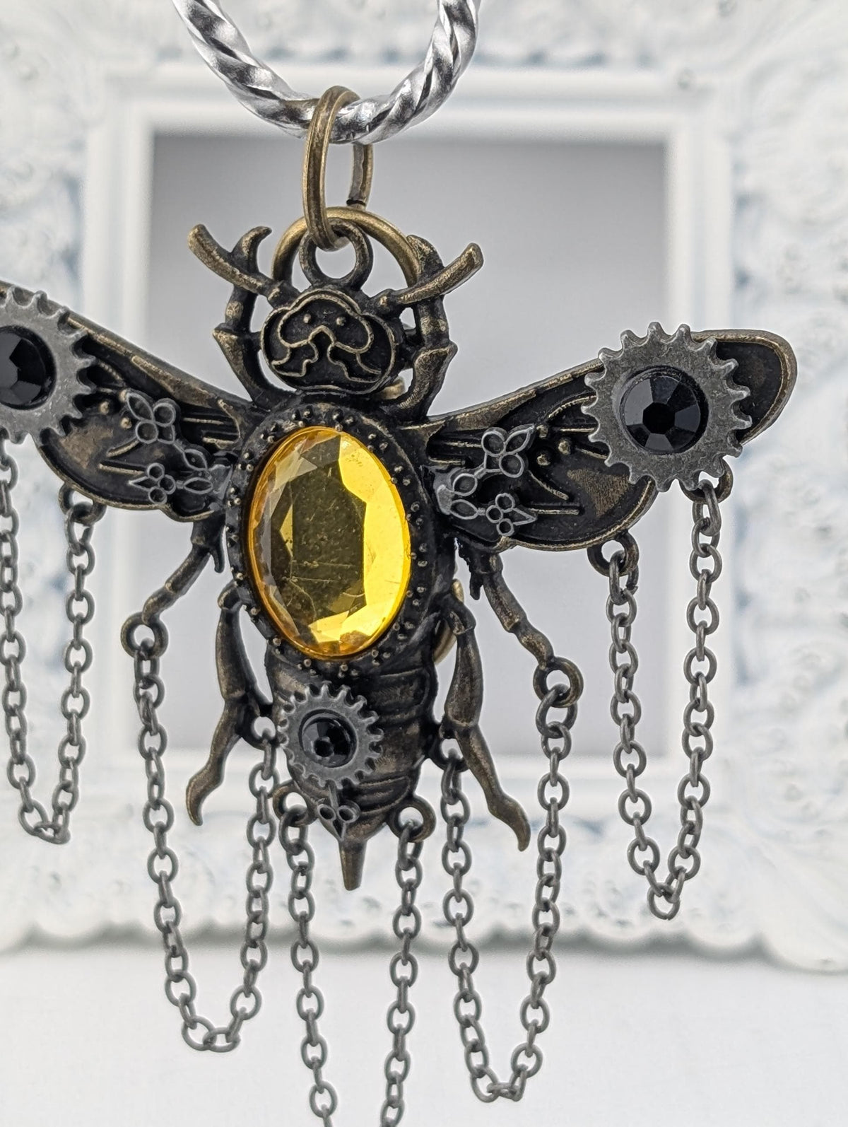 A decorative pendant in the shape of a bee, with a yellow gemstone in the center and intricate metalwork details.