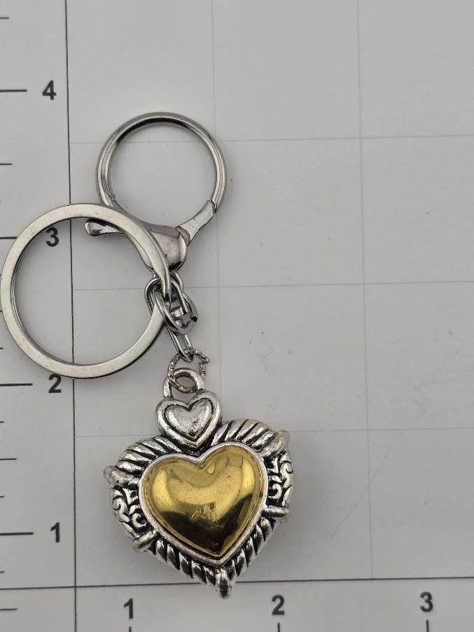 a heart-shaped pendant with a metallic, ornate design, attached to a keychain.