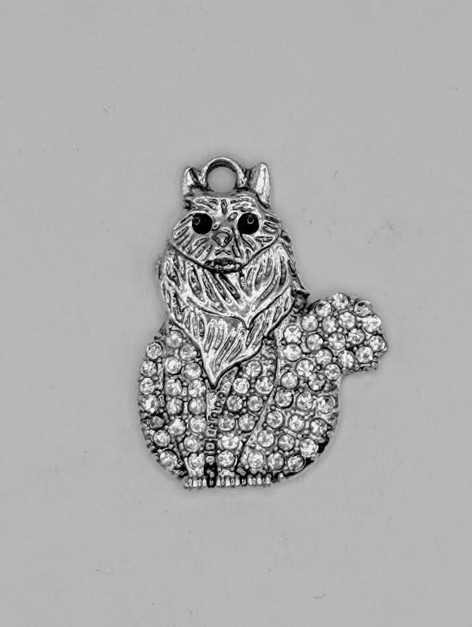 A silver-colored charm in the shape of a cat, adorned with numerous sparkling rhinestones or crystals.