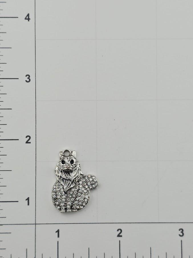 A silver-colored charm in the shape of a cat is placed on a white surface, with a ruler for scale.