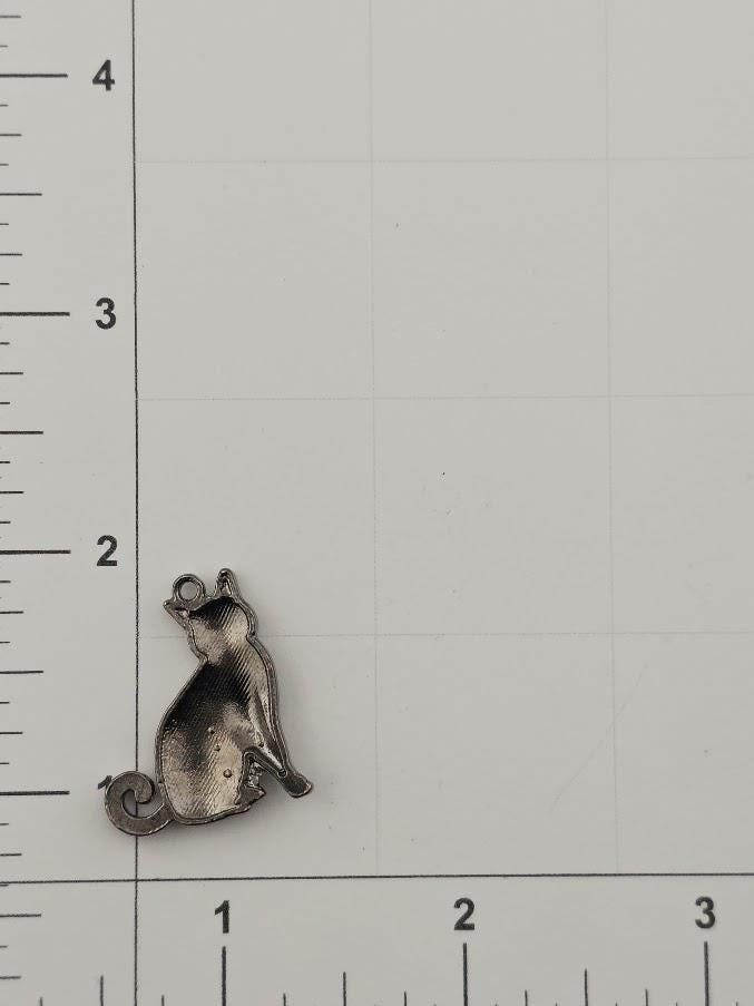 A small metal cat charm is shown on a ruler, indicating its size relative to the ruler's measurements.