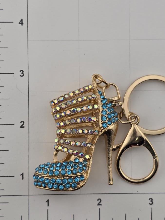 A gold-colored high-heeled shoe keychain with blue rhinestones on it, placed on a white surface with a ruler for scale.