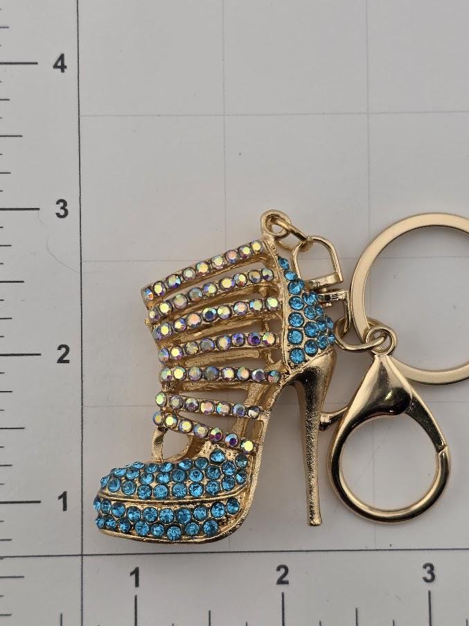 A gold-colored high-heeled shoe keychain with a blue crystal embellishment.