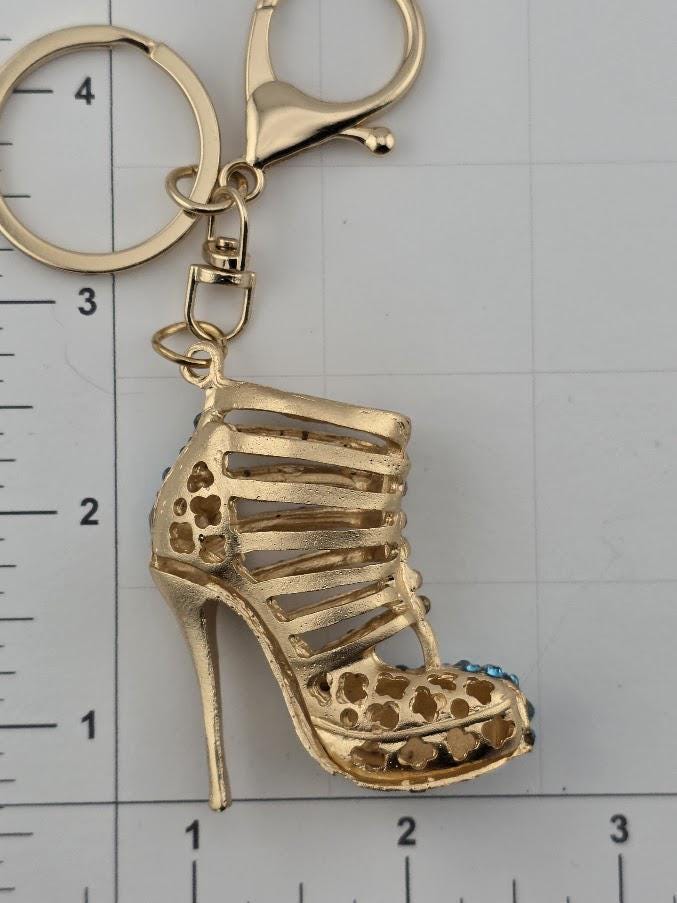 A gold-colored high-heeled shoe keychain with a decorative design and a clasp.