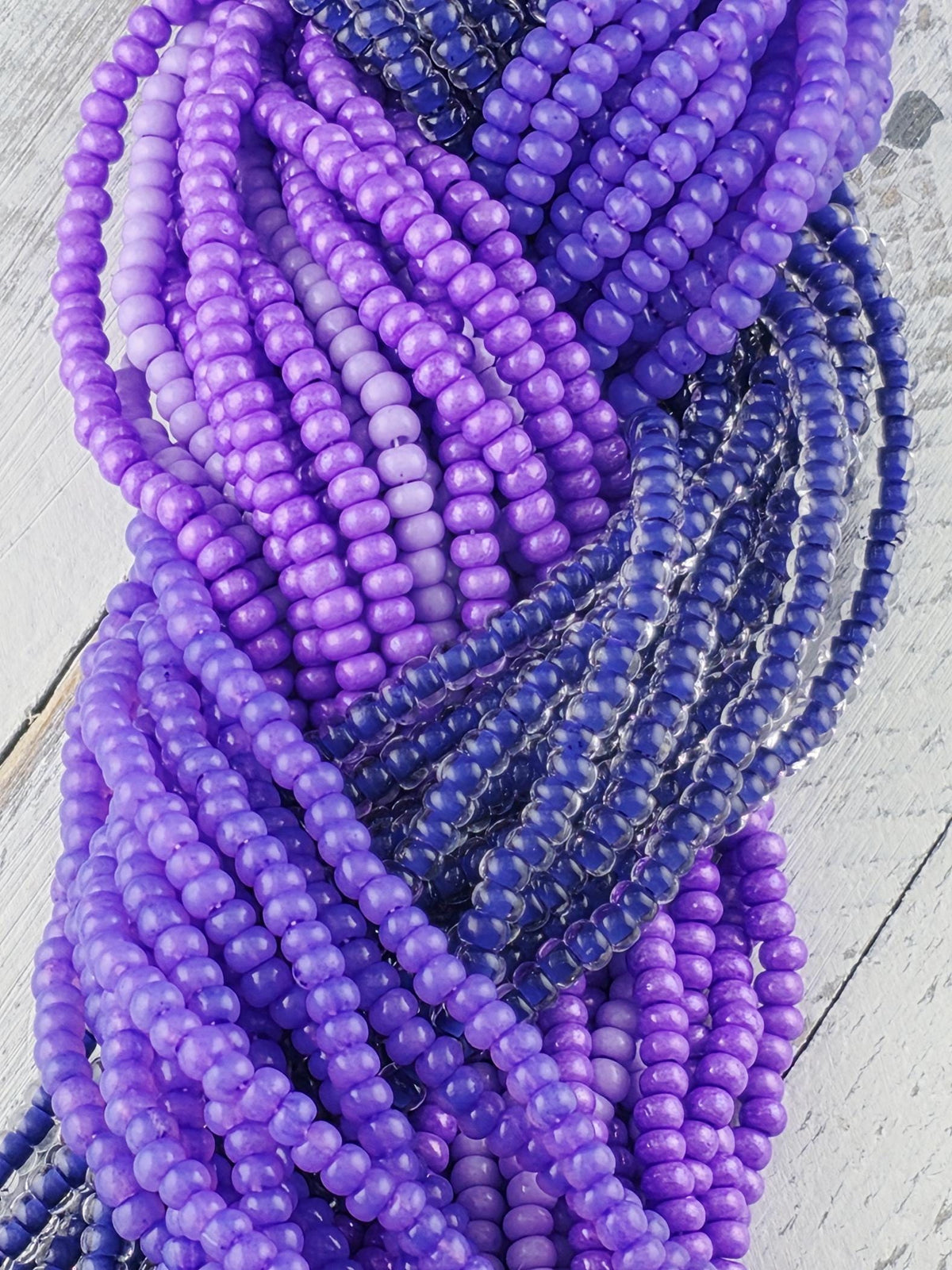 A close-up view of a collection of colorful beads, predominantly purple and blue, arranged in a tangled and intricate manner.