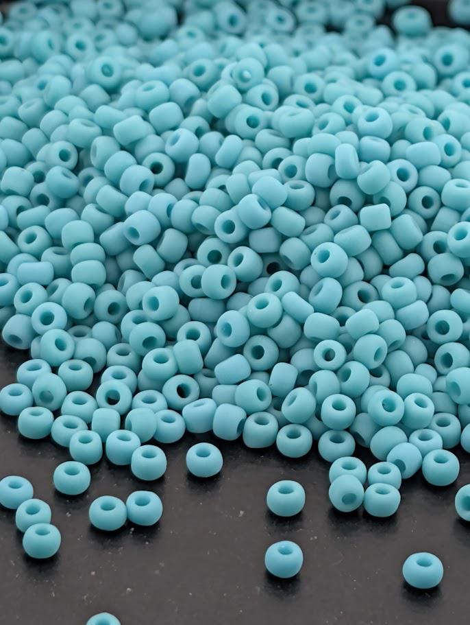 a large pile of small, light blue beads scattered on a dark surface.