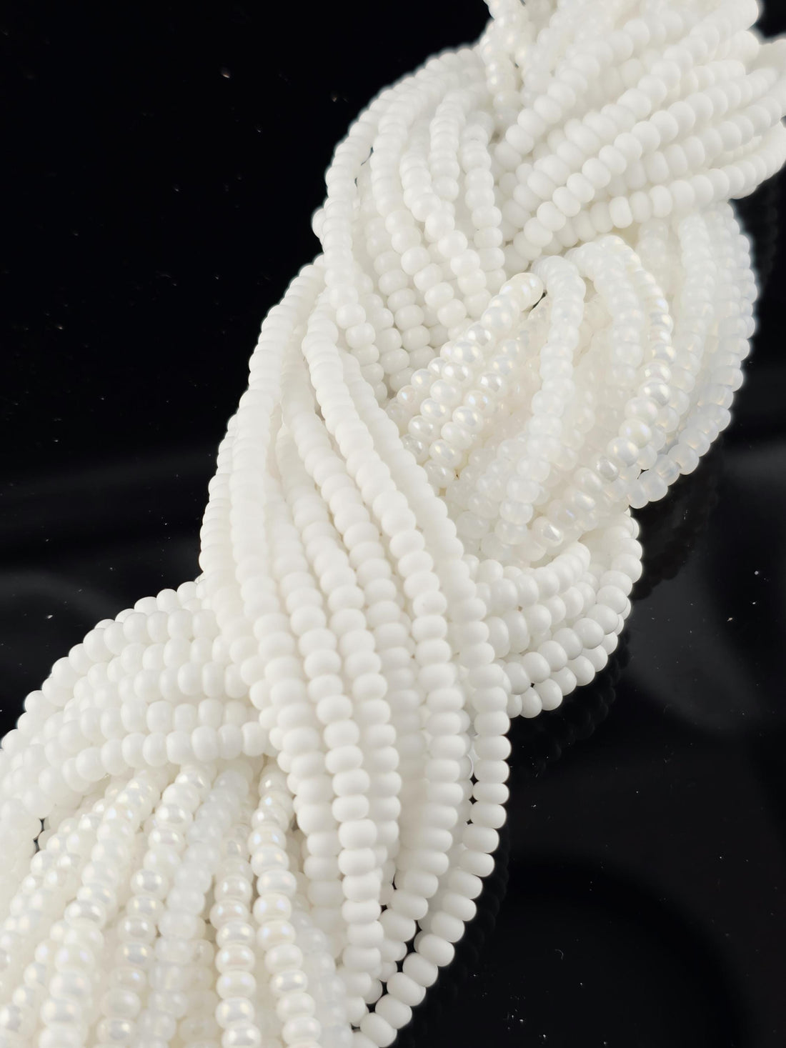 A close-up view of numerous white beads arranged in a twisted, braided pattern against a dark background.
