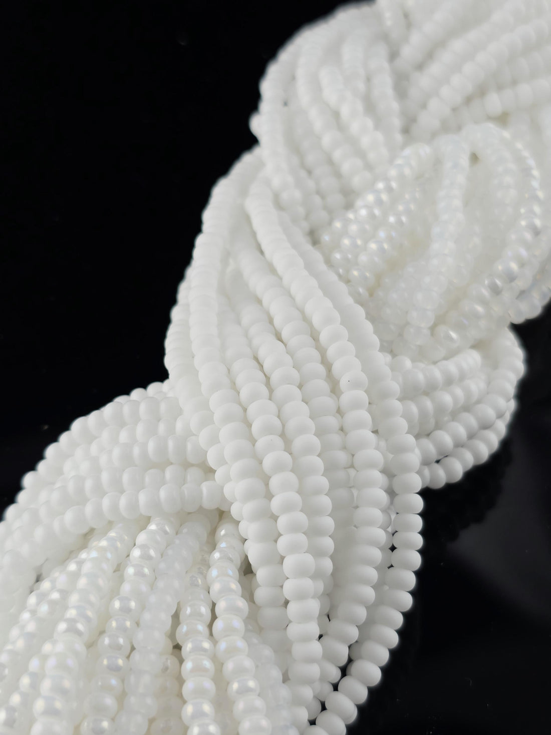 A close-up view of numerous white beads arranged in a twisted, braided pattern against a dark background.