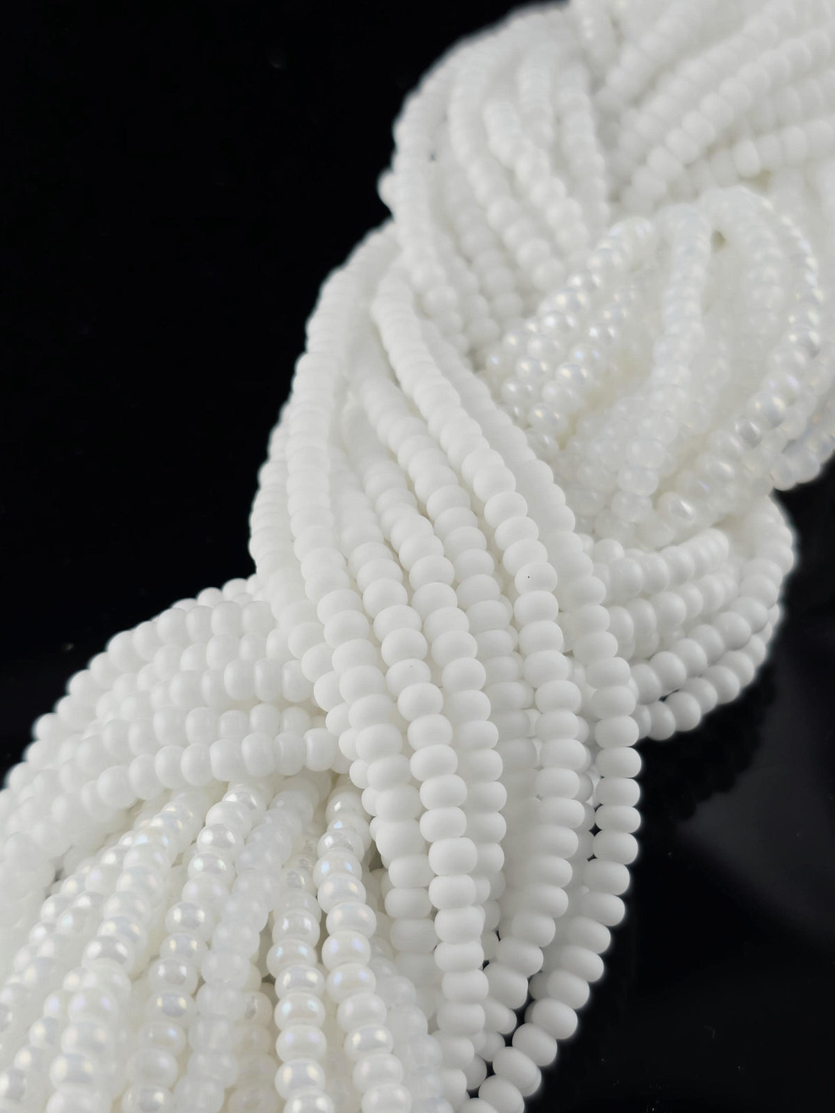 A close-up view of numerous white beads arranged in a twisted or braided pattern against a black background.