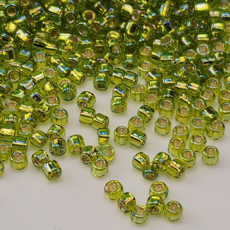 a large pile of small, green glass beads scattered on a white surface.