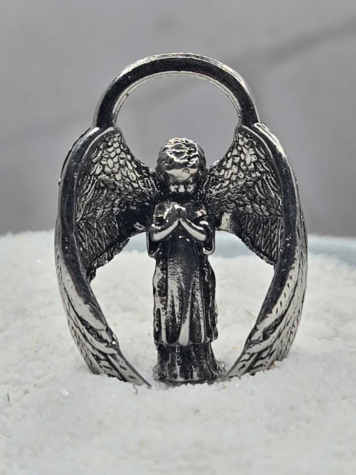 A silver-colored metal angel figurine with outstretched wings stands on a snowy surface.