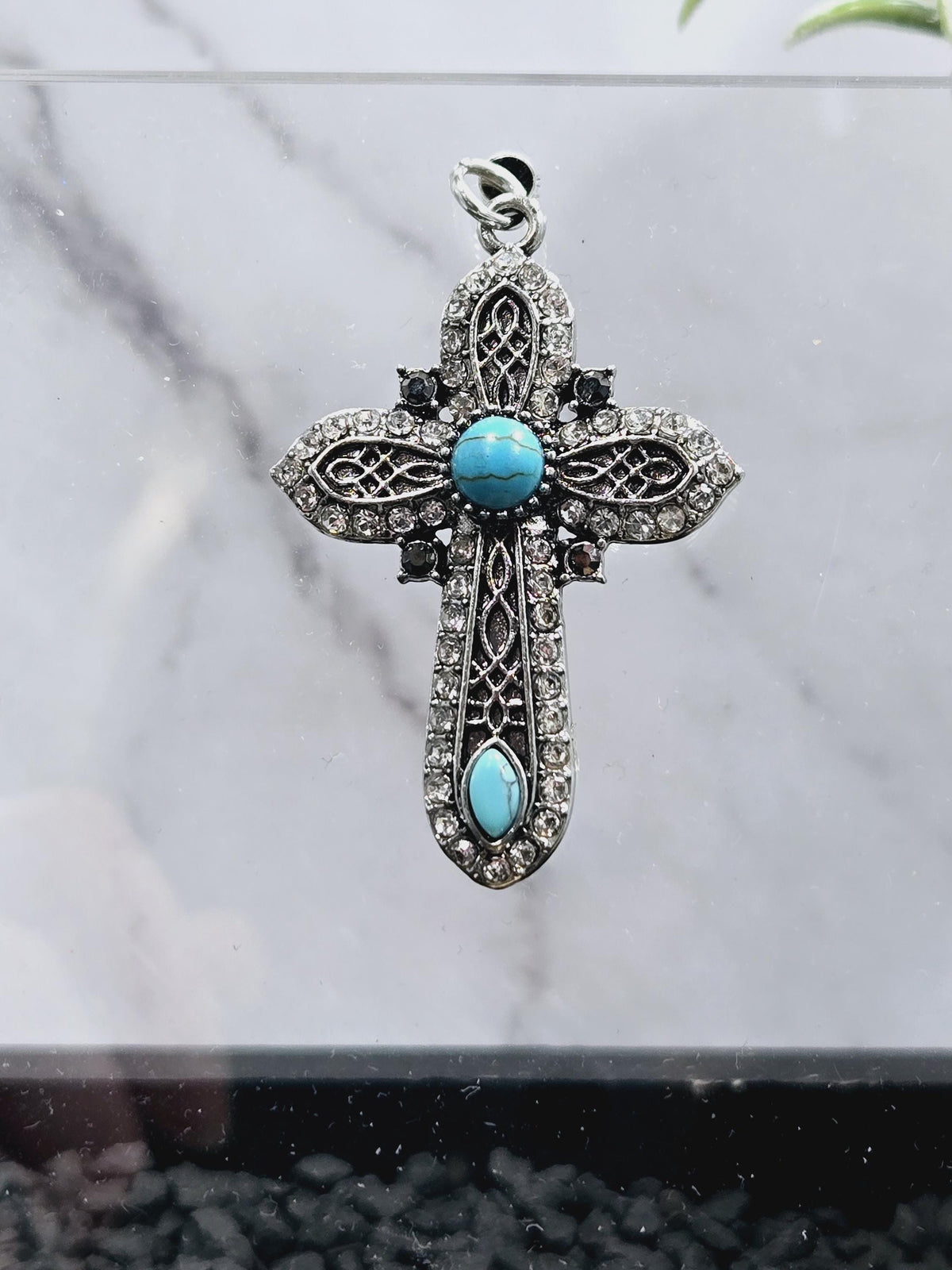 A decorative cross pendant with turquoise stones and sparkling rhinestones.