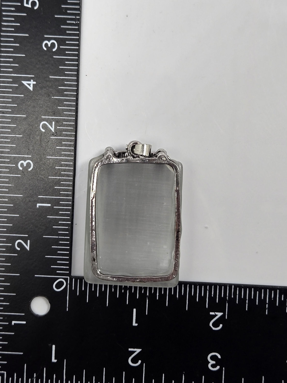 A silver-colored rectangular object is placed next to a ruler on a white surface.