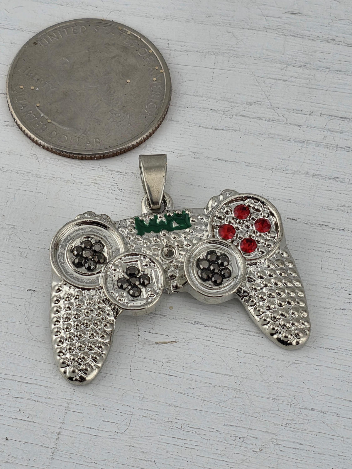 A silver pendant in the shape of a video game controller, adorned with red gemstones, is placed next to a United States quarter.