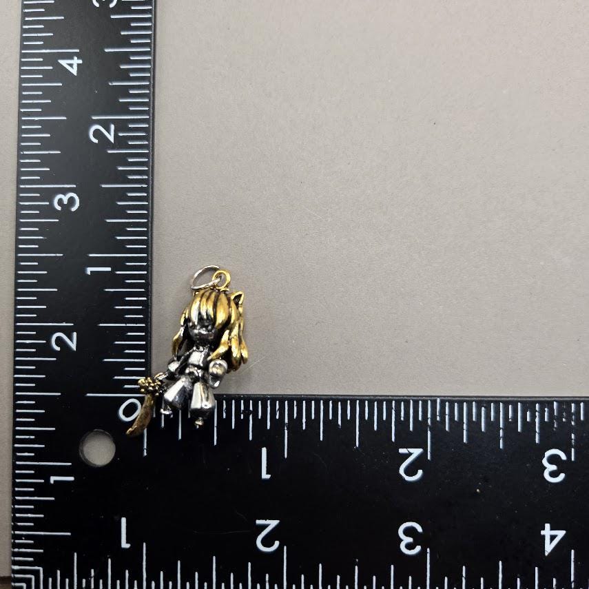 A small, gold-colored charm or pendant is placed next to a ruler on a gray surface.