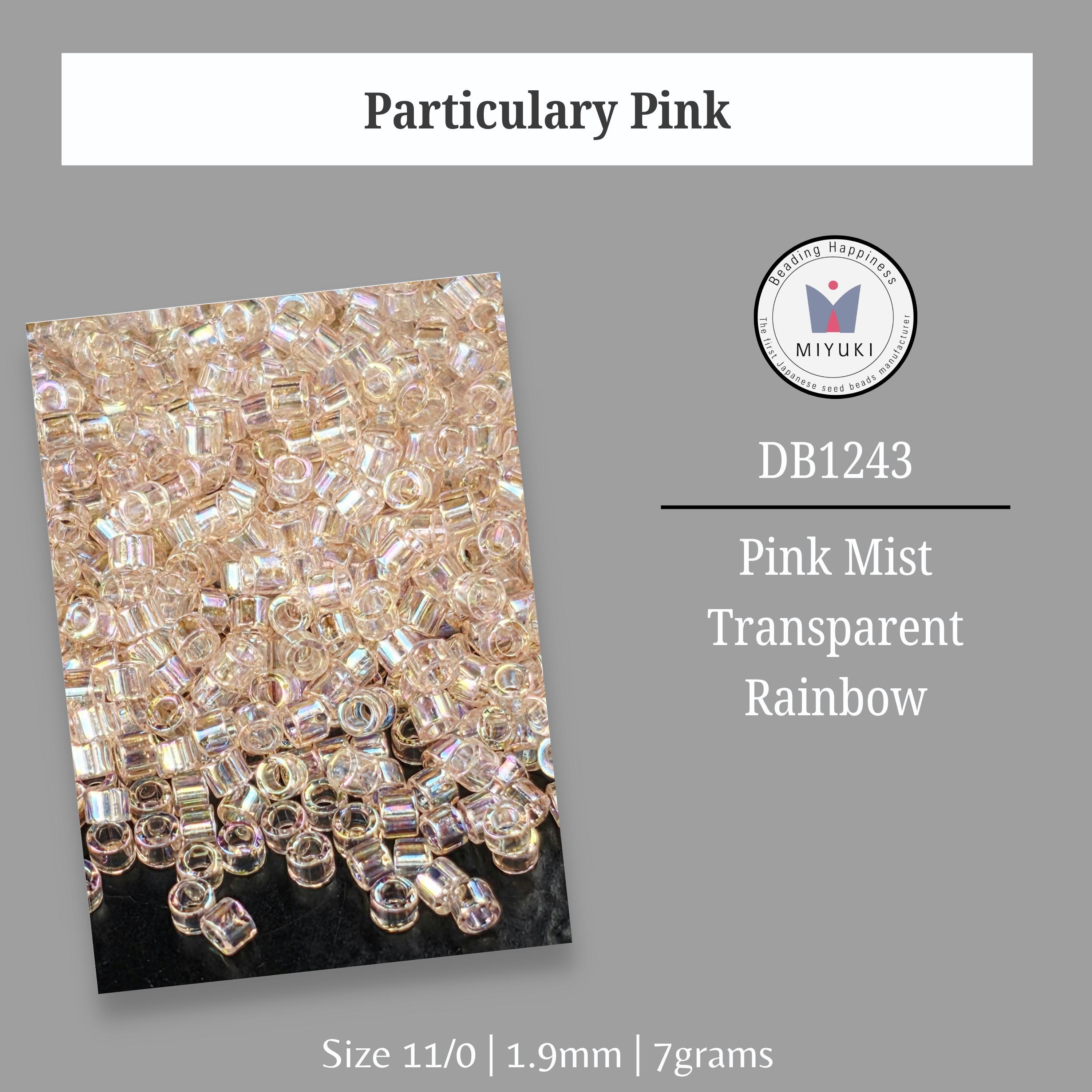 a collection of transparent, rainbow-colored beads or crystals, possibly in the form of a pink mist. The image is labeled with the text "Particular Pink" and "DB1243 Pink Mist Transparent Rainbow" along with the size "Size 11/0 | 1.9mm | 7grams".
