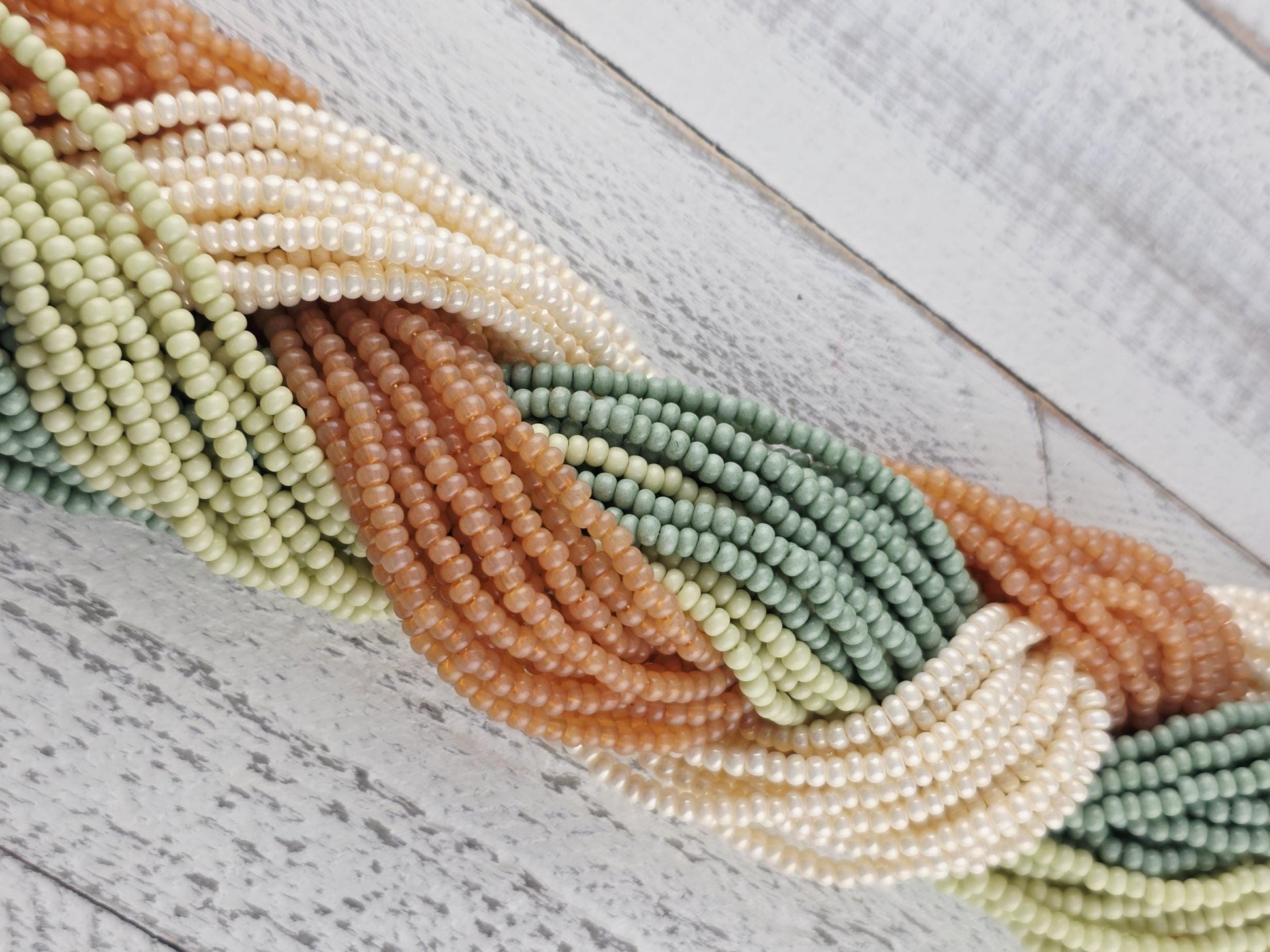 A close-up view of a collection of colorful beads, including green, white, orange, and brown beads, arranged in a twisted pattern on a wooden surface.