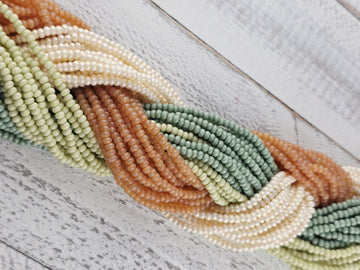 A close-up view of a collection of colorful beads, including green, white, orange, and brown beads, arranged in a twisted pattern on a wooden surface.