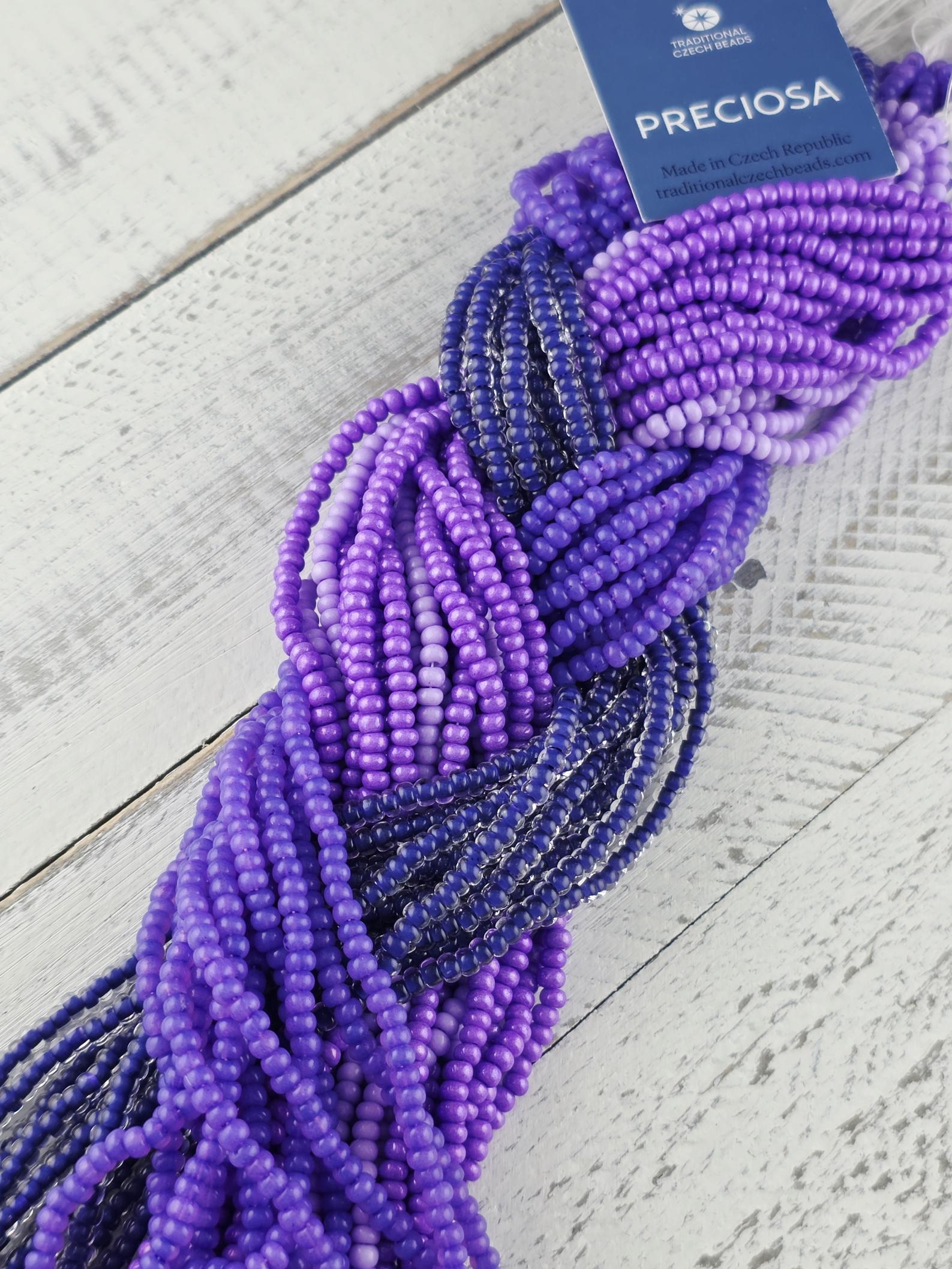 A close-up view of a collection of colorful beads, predominantly purple and blue, arranged in a twisted pattern on a wooden surface.