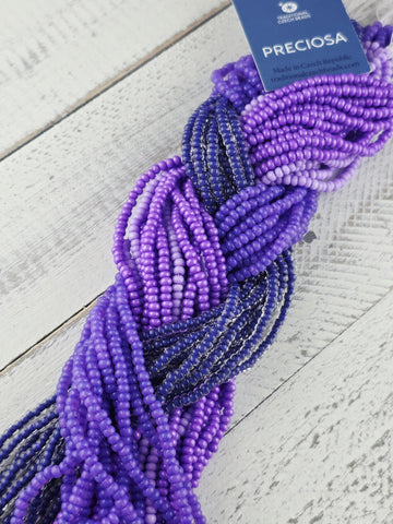 A close-up view of a collection of colorful beads, predominantly purple and blue, arranged in a twisted pattern on a wooden surface.